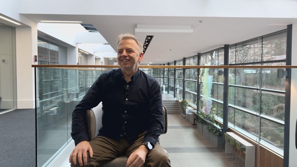 Co-founder Mark sat in a chair, with a modern glass building interior